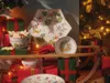 Christmas-themed tableware and gifts arranged on a wooden sled, with a decorated Christmas tree in the background. Produktbild-Vorschau