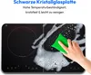 A hand is cleaning a black induction cooktop with a green sponge and soap suds. Produktbild-Vorschau