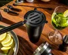 A collection of bar tools and a cocktail are arranged on a wooden table. Voir les images du produit