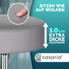A close-up view of a gray stool cushion with a finger pressing into it, highlighting its softness. Produktbild-Vorschau
