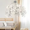 A pendant lamp with white leaf-like elements hangs above a wooden sofa with cushions. Produktbild-Vorschau