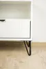 A close-up shot of the bottom part of a white cabinet with black hairpin legs. Podgląd zdjęcia produktu