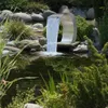 A garden pond with a modern stainless steel waterfall feature surrounded by rocks and lush greenery. Produktbild-Vorschau