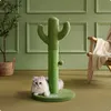 A cat is lying on the floor next to a cactus-shaped cat scratching post in a room with green walls and a wooden chair in the background. Produktbild-Vorschau