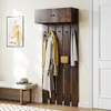 A wall-mounted coat rack with a cabinet above, featuring coats, scarves, and a bag hanging on hooks, with a bench and artwork in the background. Náhled obrázku produktu