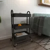 A black three-tiered rolling cart is shown next to a teal sofa in a room with wooden floors and a rug. Voir les images du produit
