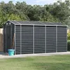 A dark gray metal shed with a silver roof and trim, situated on a concrete pad in a grassy yard with trees in the background. Náhled obrázku produktu
