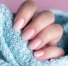A close-up of a hand with light pink gel nails, resting on a light blue knitted fabric. Anteprima dell’immagine prodotto