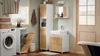 A modern bathroom with a washing machine, laundry basket, vanity, and a tall cabinet. Voir les images du produit