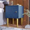 A blue nightstand with gold legs is placed next to a bed, with a wooden wall in the background. Podgląd zdjęcia produktu