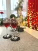 Two wine glasses filled with red wine are placed on a grey felt table runner, with a Christmas tree and red curtains with fairy lights in the background. Produktbild-Vorschau