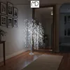 A decorative LED willow tree with lights and star accents stands in a hallway next to a large mirror. Framed pictures hang on the wall. Podgląd zdjęcia produktu