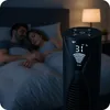 A couple sleeping in bed at night, with a tower fan in the foreground displaying a temperature reading of 31°C. Náhled obrázku produktu