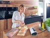 A woman is in a kitchen preparing fish, with a vacuum sealer on the counter. Náhľad obrázku produktu