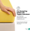 A hand is shown pressing down on a yellow fitted sheet that is placed on a mattress. Produktbild-Vorschau