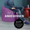 A person is sitting on a purple beanbag chair in a room. Produktbild-Vorschau