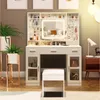 A white vanity table with a lighted mirror, drawers, and shelves, filled with makeup and skincare products. A white stool is placed in front of the table. Voir les images du produit