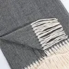A close-up view of a folded grey herringbone blanket with cream-colored fringe. Anteprima dell’immagine prodotto
