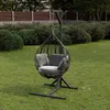 A hanging chair with cushions sits on a green lawn in a garden setting, with bushes and a fence in the background. Podgląd zdjęcia produktu