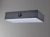 A modern, rectangular outdoor light fixture with a dark top and a translucent bottom, mounted on a gray wall. Produktbild-Vorschau