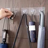 A hand is hanging keys on a clear adhesive hook on a wooden wall. Several other hooks hold bags and umbrellas. Produktbild-Vorschau