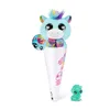 A light blue plush unicorn toy peeking out of a white cone-shaped packaging, with a small green toy figure in front of it. Podgląd zdjęcia produktu