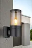 An outdoor wall lamp is mounted on a concrete wall next to a modern building. Náhled obrázku produktu