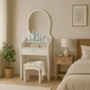 A bedroom scene featuring a white vanity table with a mirror, a stool, and a bedside table with a lamp. Voir les images du produit