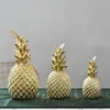 Three golden pineapple ornaments of varying sizes are displayed on a dark green cloth. Produktbild-Vorschau