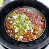 A round metal grill plate filled with food, including potatoes, tomatoes, cheese, and sliced steak, is placed on a grill. Podgląd zdjęcia produktu
