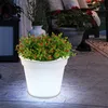 A glowing white planter with a green plant and red berries sits on a stone patio at night. Produktbild-Vorschau