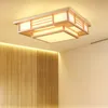 A modern wooden ceiling light fixture with a Japanese design, illuminated against a plain ceiling and a wood-paneled wall. Náhled obrázku produktu