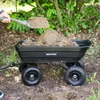 A person is using a shovel to put dirt into a black garden cart. Náhled obrázku produktu