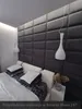 A bedroom scene with upholstered wall panels behind a bed. The room has modern pendant lights and decorative pillows. Produktbild-Vorschau