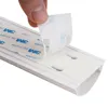 A hand is peeling off the backing from the adhesive strip on a white PVC cable channel. Produktbild-Vorschau
