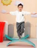 A young girl is balancing on a turquoise wobble board in a playroom. Podgląd zdjęcia produktu