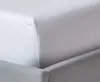 A close-up view of a white fitted sheet draped over a gray bed skirt. Produktbild-Vorschau