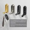 Four foldable wall hooks are displayed on a textured gray wall. The hooks are in different colors: gold, silver, dark gray, and black. A set of keys with a braided strap is hanging from the gold hook. Text is overlaid on the bottom right of the image. Produktbild-Vorschau