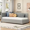 A daybed with several decorative pillows is shown in a well-lit room with large windows and a rug. Produktbild-Vorschau