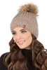 A woman wearing a beige knitted hat with a pom-pom and a black turtleneck. Náhled obrázku produktu