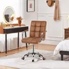 A brown faux leather office chair is placed in a room with a vanity table and a bed. Produktbild-Vorschau
