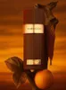 A perfume bottle is displayed with natural elements like wood, honeycomb, leaves, and an orange. Voir les images du produit