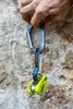 Hand hält schwarzen Karabiner mit schwarzem und weißem Band und gelbem Sicherungsgerät Ohmega von Edelrid vor Felswand Podgląd zdjęcia produktu
