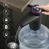 A person's hand is pressing a button on a black water dispenser pump attached to a large water bottle. Water is being dispensed into a glass. Náhled obrázku produktu