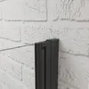 A close-up view of a black framed shower door with a glass panel against a white brick wall. Produktbild-Vorschau