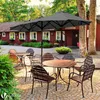 An outdoor patio scene with tables and chairs under a large umbrella, in front of a red building. Produktbild-Vorschau