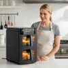 A woman in an apron stands next to a black double-chamber air fryer in a kitchen setting. Produktbild-Vorschau