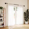 A living room scene with sheer white curtains covering a glass door, a black curtain rod, a bookshelf with decor, and a potted plant. Podgląd zdjęcia produktu