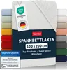 A white fitted sheet is displayed prominently, with a stack of sheets in various colors visible on the left and right sides. Several tags and certifications are attached to the sheet. Produktbild-Vorschau