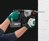 A person wearing gloves is using a cordless hammer drill to drill into a white brick wall. Produktbild-Vorschau